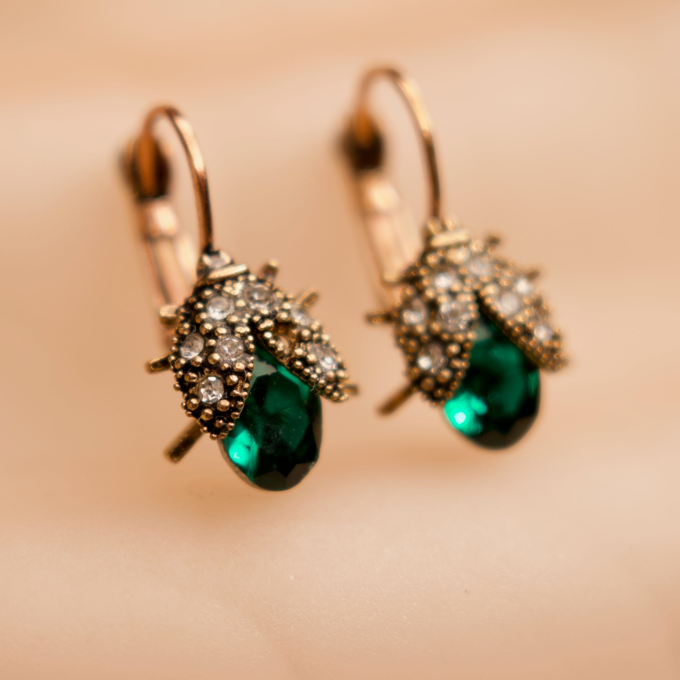 Pair of earrings with green gemstones and gold accents on a blurred background