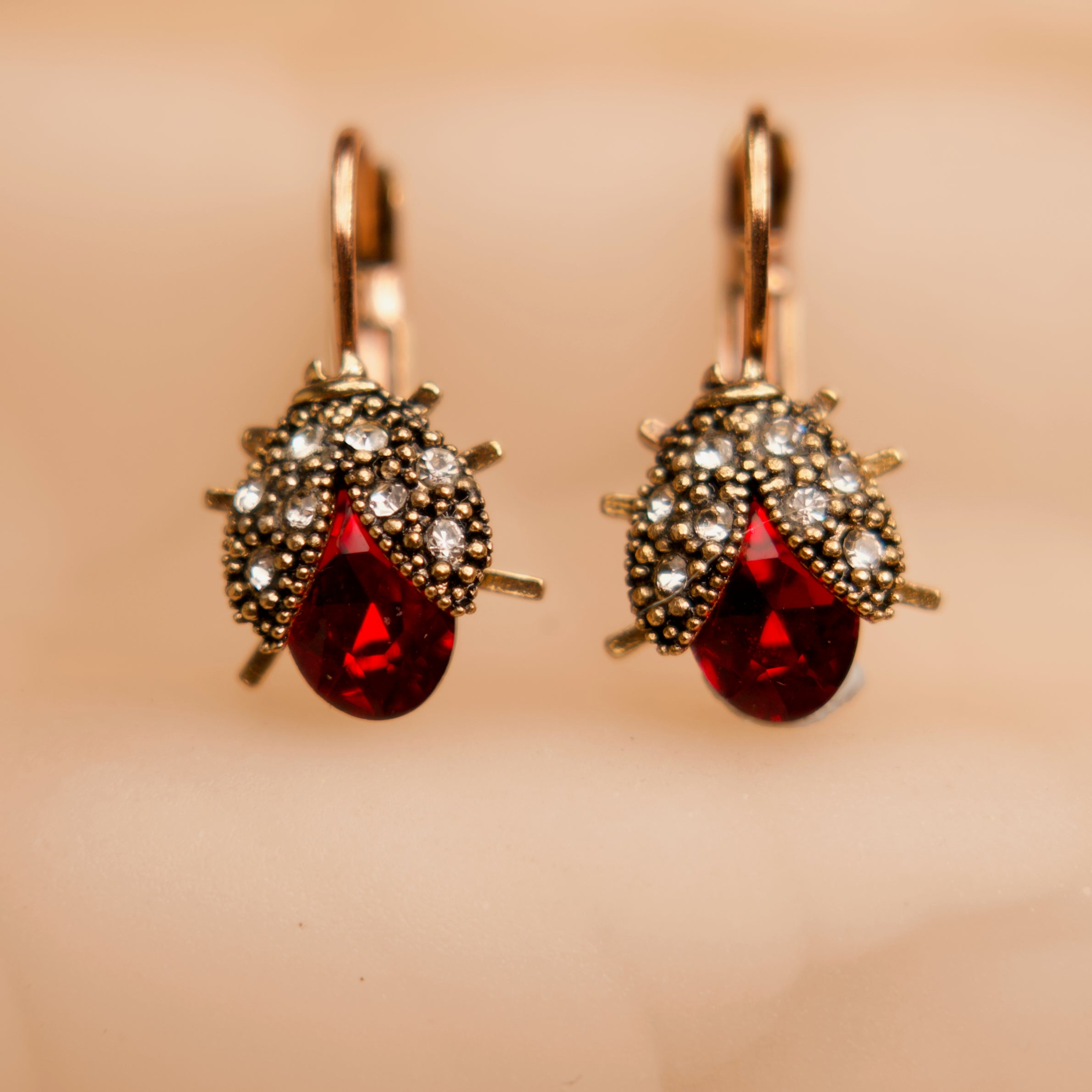 Pair of earrings with red teardrop stones and gold accents on a beige background