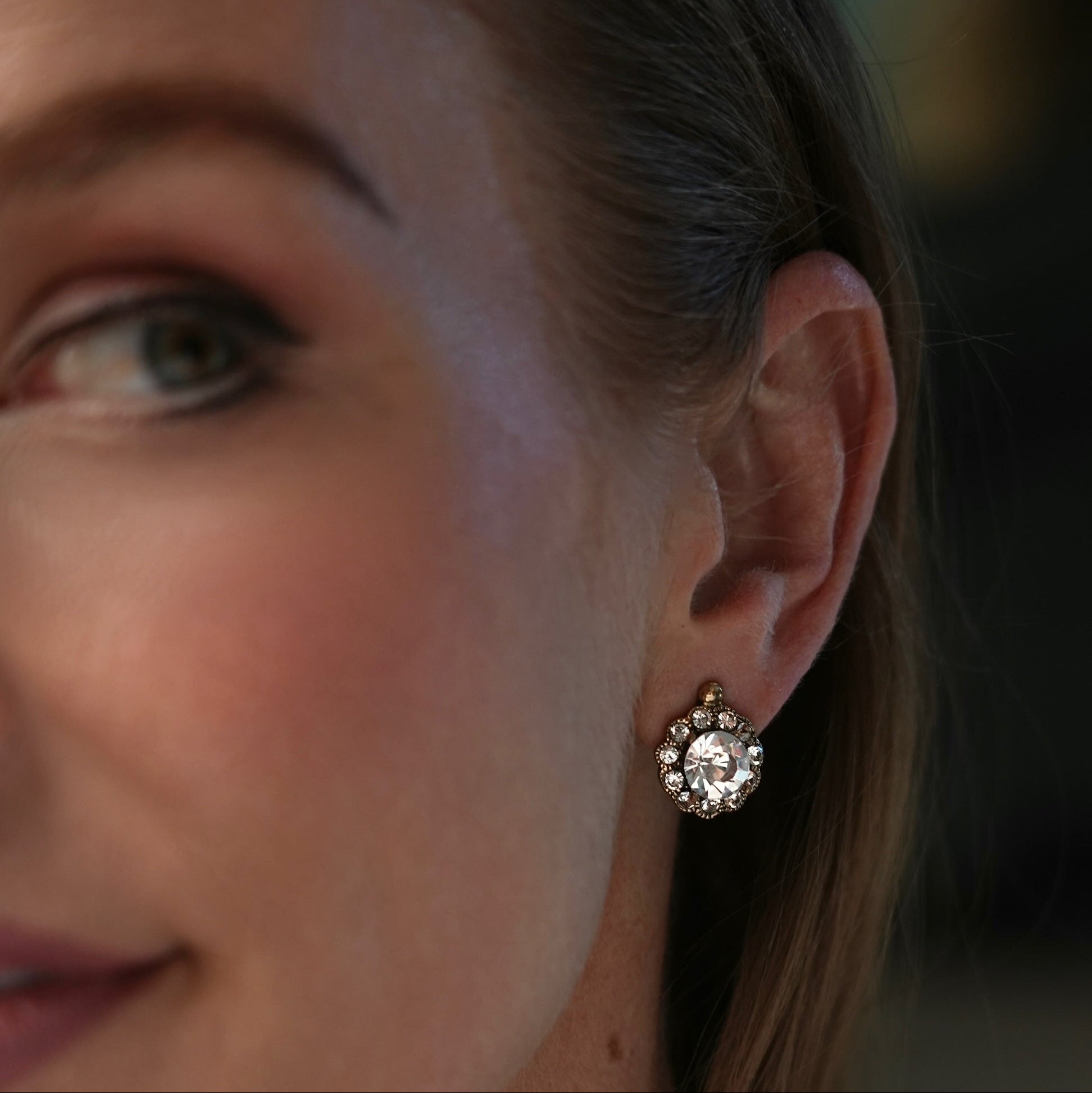 Close-up of a woman's ear wearing a decorative earring with a blurred background