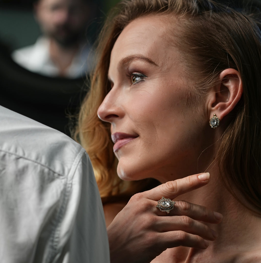 Close-up of a woman wearing a diamond ring and earrings, with a blurred background.