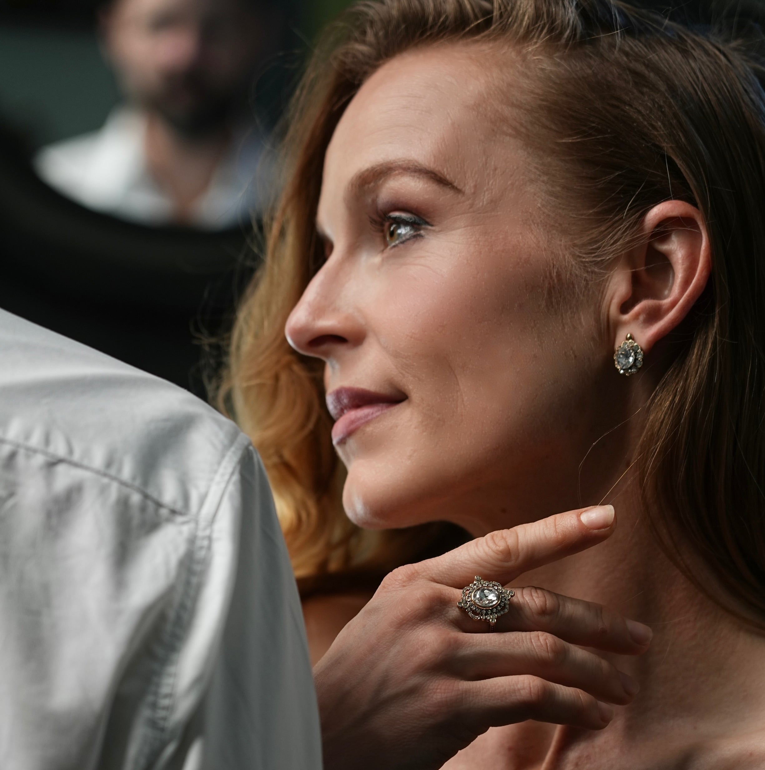 Close-up of a woman wearing a diamond ring and earrings, with a blurred background.