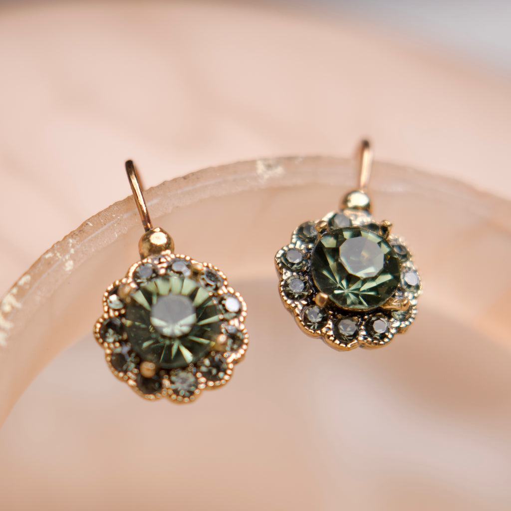 Pair of earrings with green gemstones on a soft pink background
