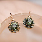 Pair of earrings with green gemstones on a soft pink background