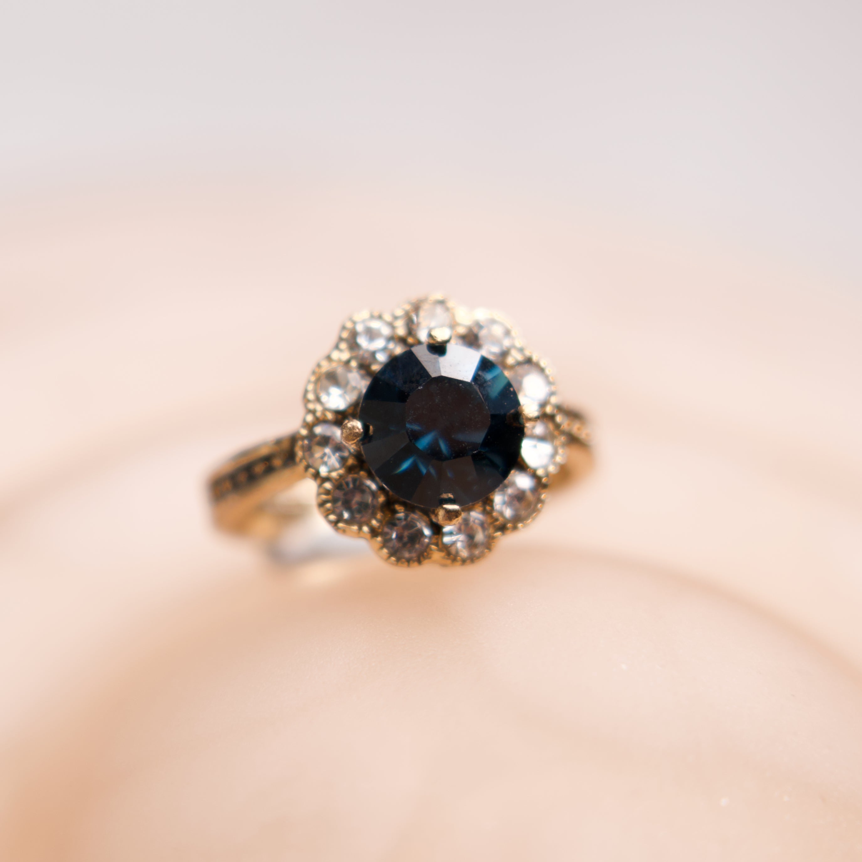 Ring with a blue gemstone and diamond-studded halo on a soft pink background