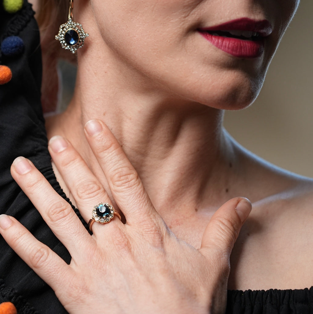 Woman wearing a black dress with colorful pom-poms, holding her hand near her face, with a close-up of her jewelry.