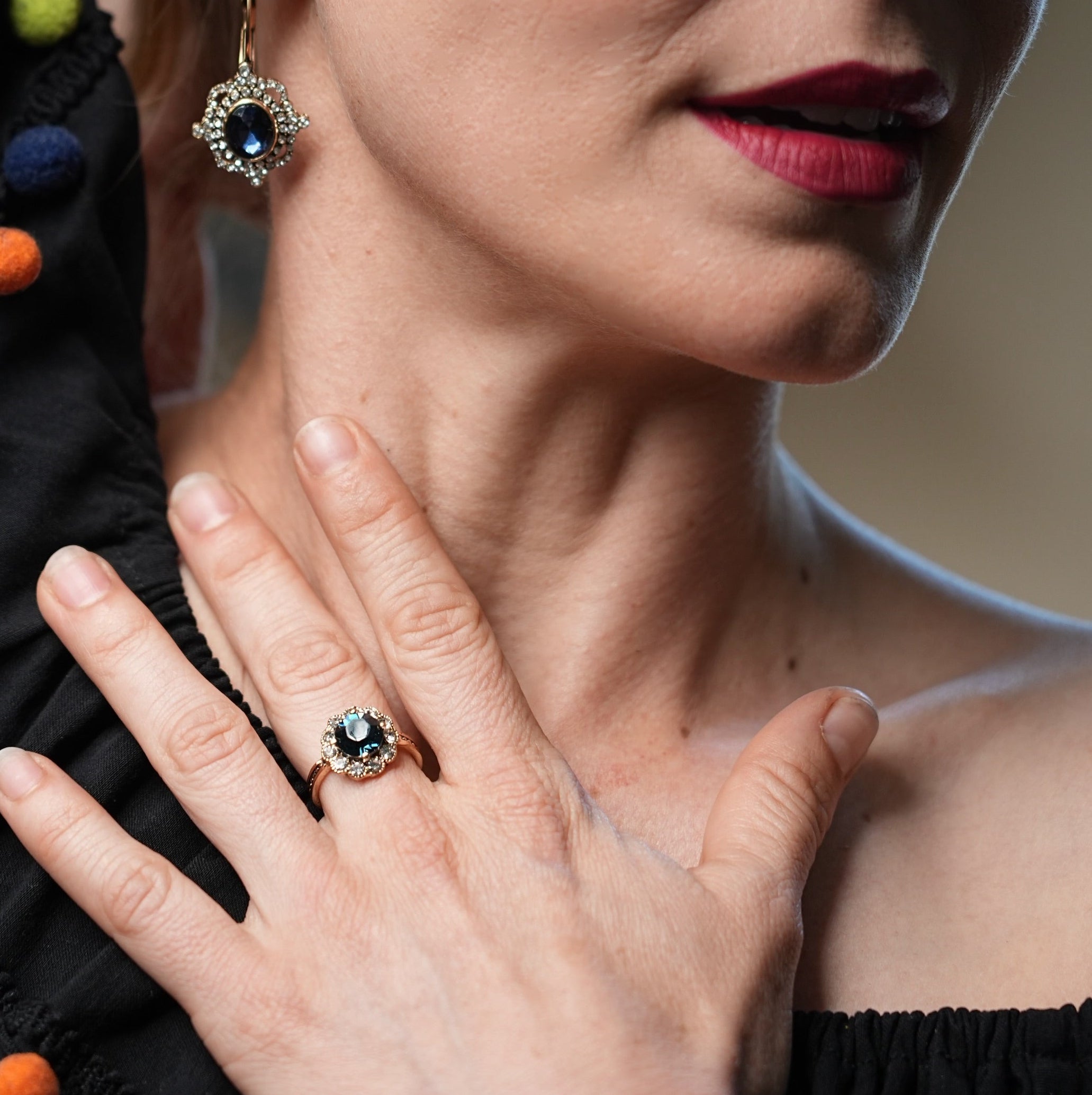 Woman wearing a black dress with colorful pom-poms, holding her hand near her face, with a close-up of her jewelry.