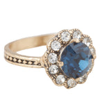 Gold ring with a blue gemstone and smaller clear stones on a white background