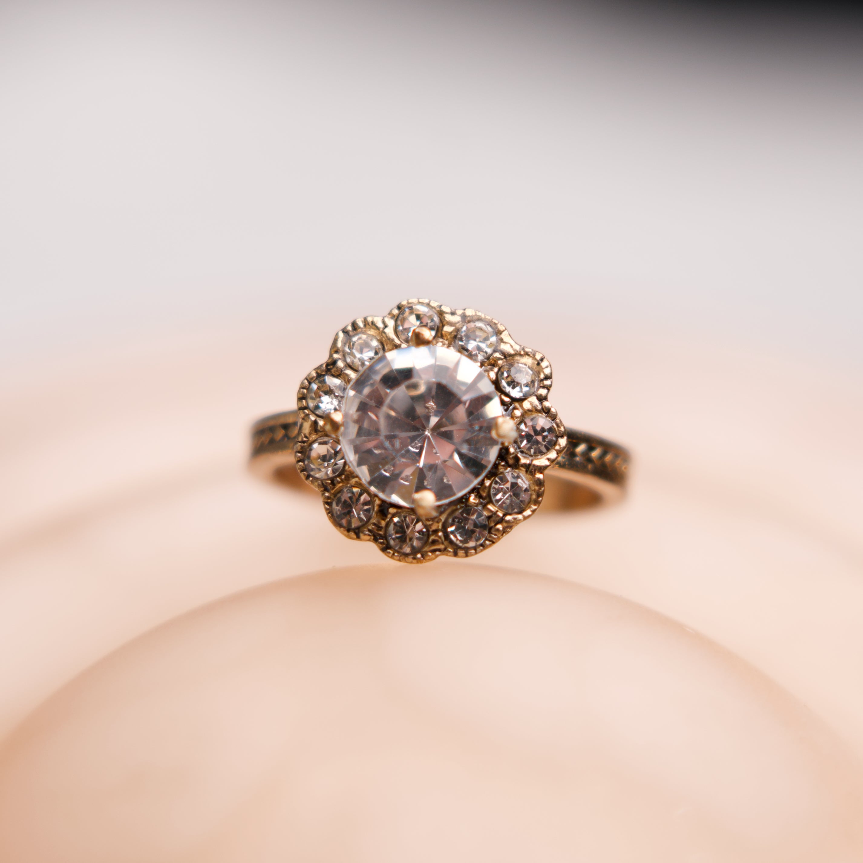 Gold ring with a large diamond and smaller stones on a soft beige background