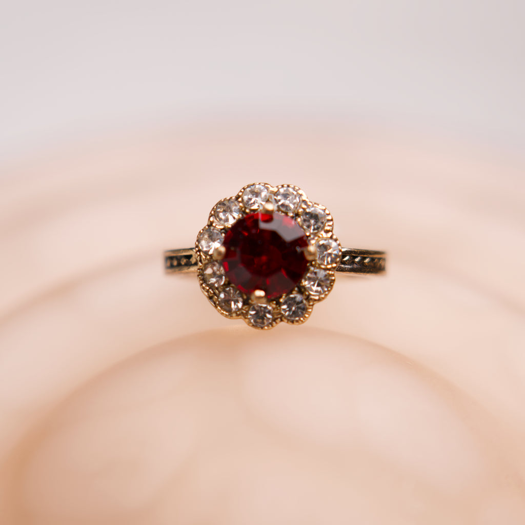 Ring with a red gemstone and diamond accents on a soft pink background