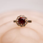 Ring with a red gemstone and diamond accents on a soft pink background