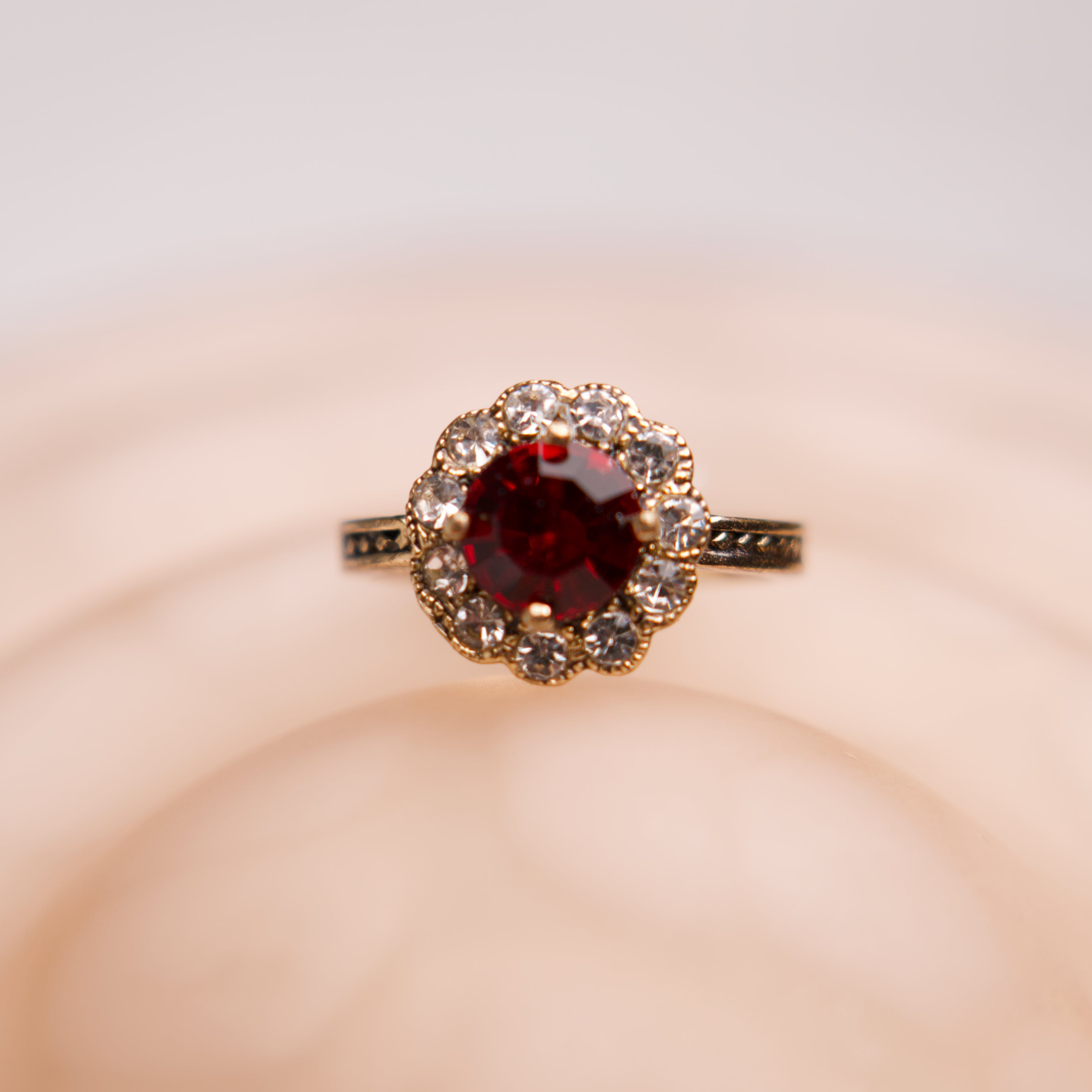 Ring with a red gemstone and diamond accents on a soft pink background
