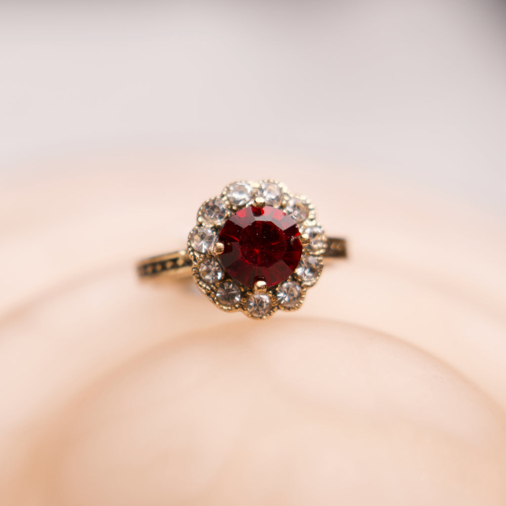 Ring with a red gemstone and diamond accents on a soft pink background