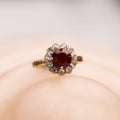 Ring with a red gemstone and diamond accents on a soft pink background
