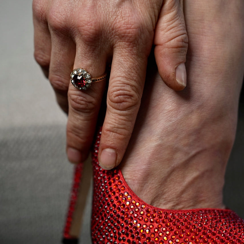 Close-up of a hand holding a red high-heeled shoe with sparkling details.