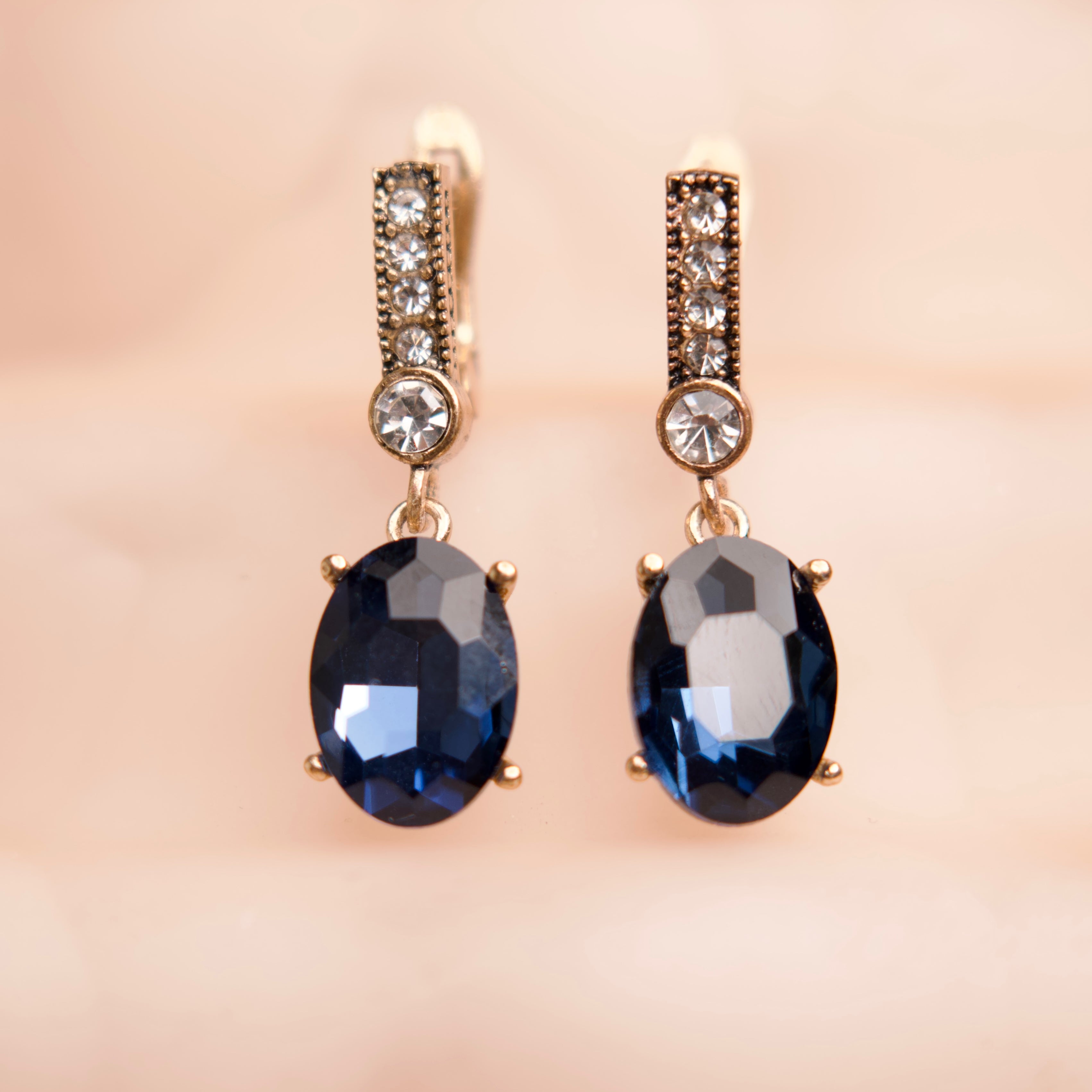 Pair of gold earrings with blue gemstones on a beige background