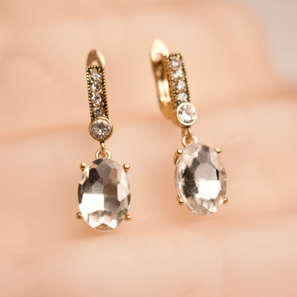 Gold earrings with clear gemstones on a soft pink background