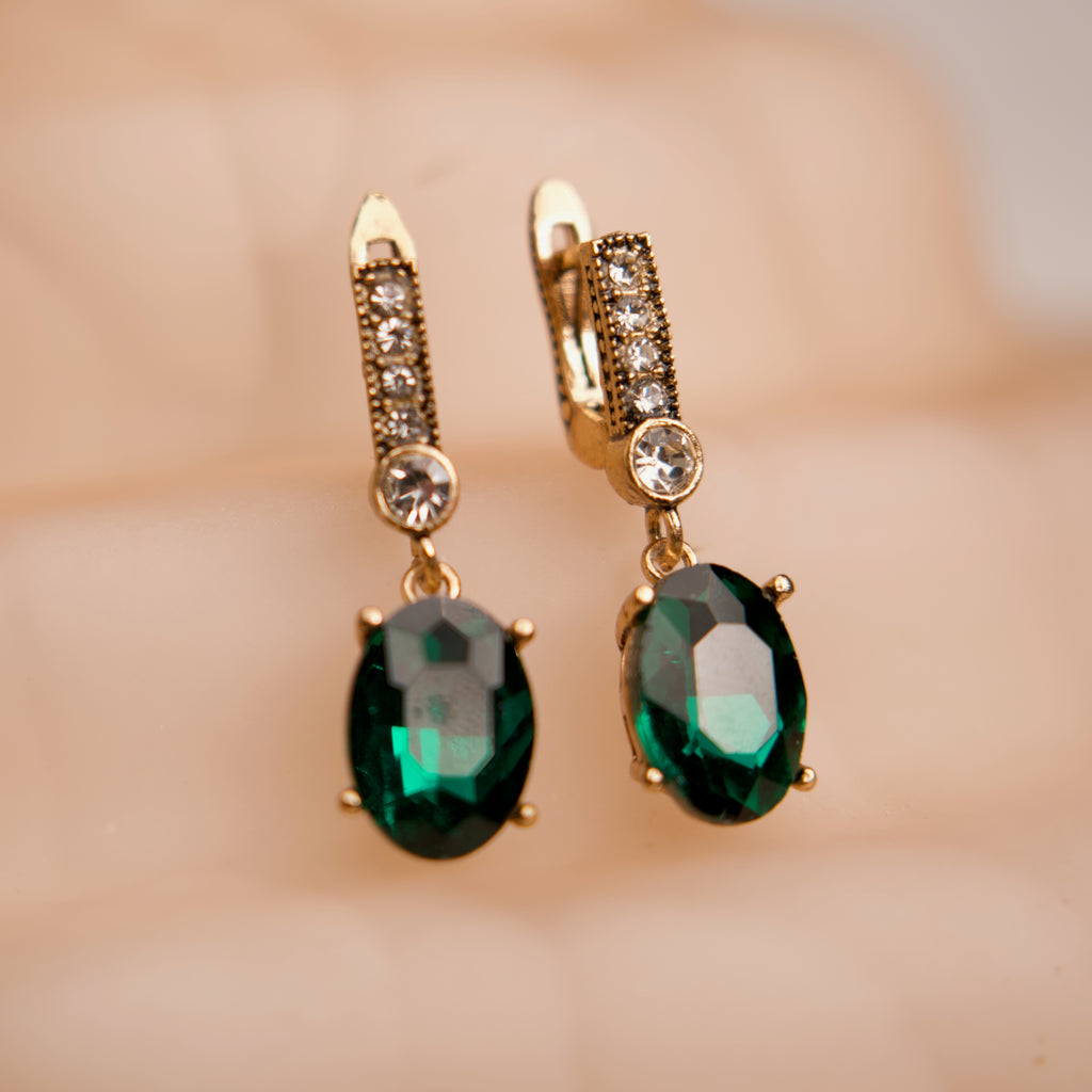 Gold earrings with green gemstones on a blurred background