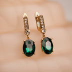 Gold earrings with green gemstones on a blurred background