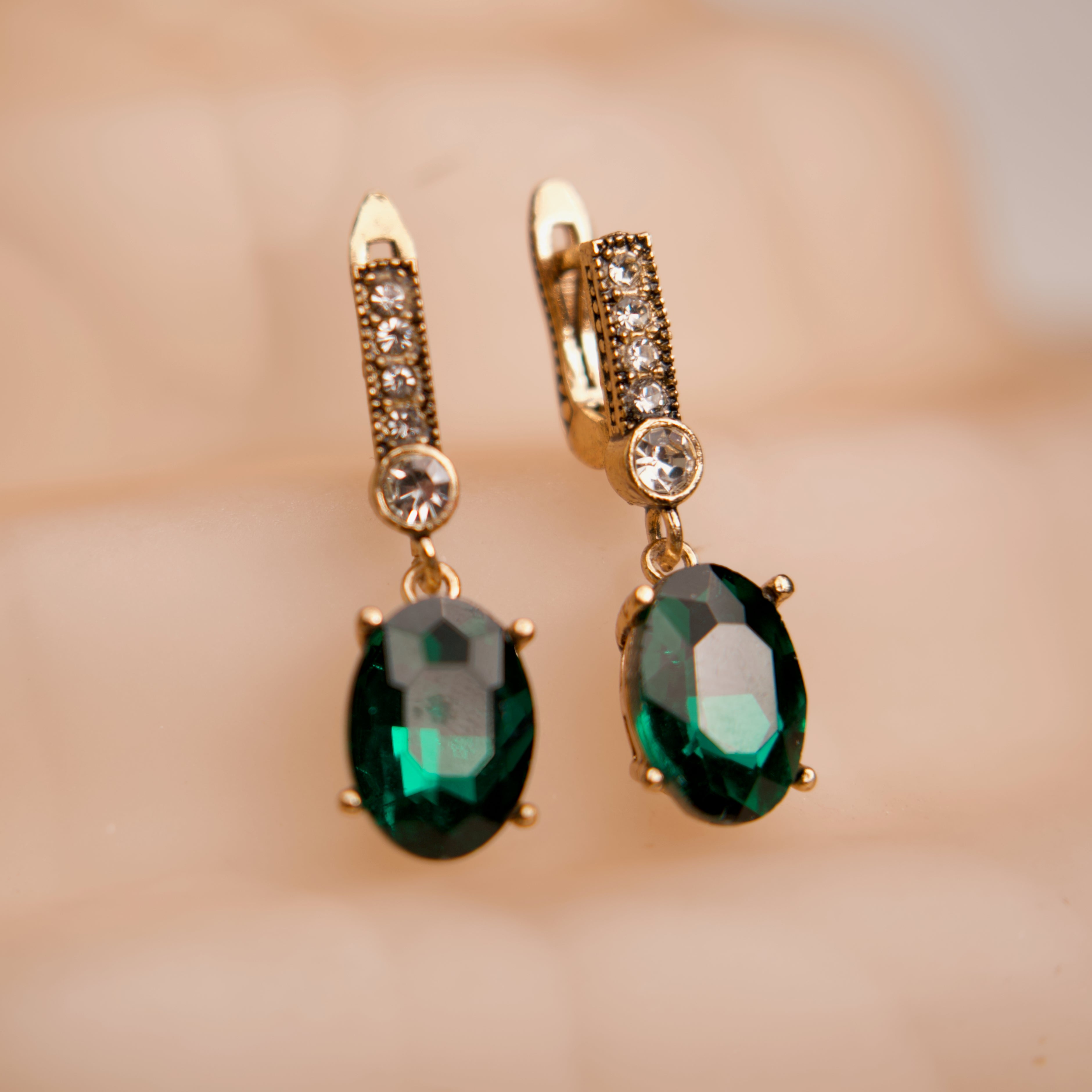 Gold earrings with green gemstones on a blurred background