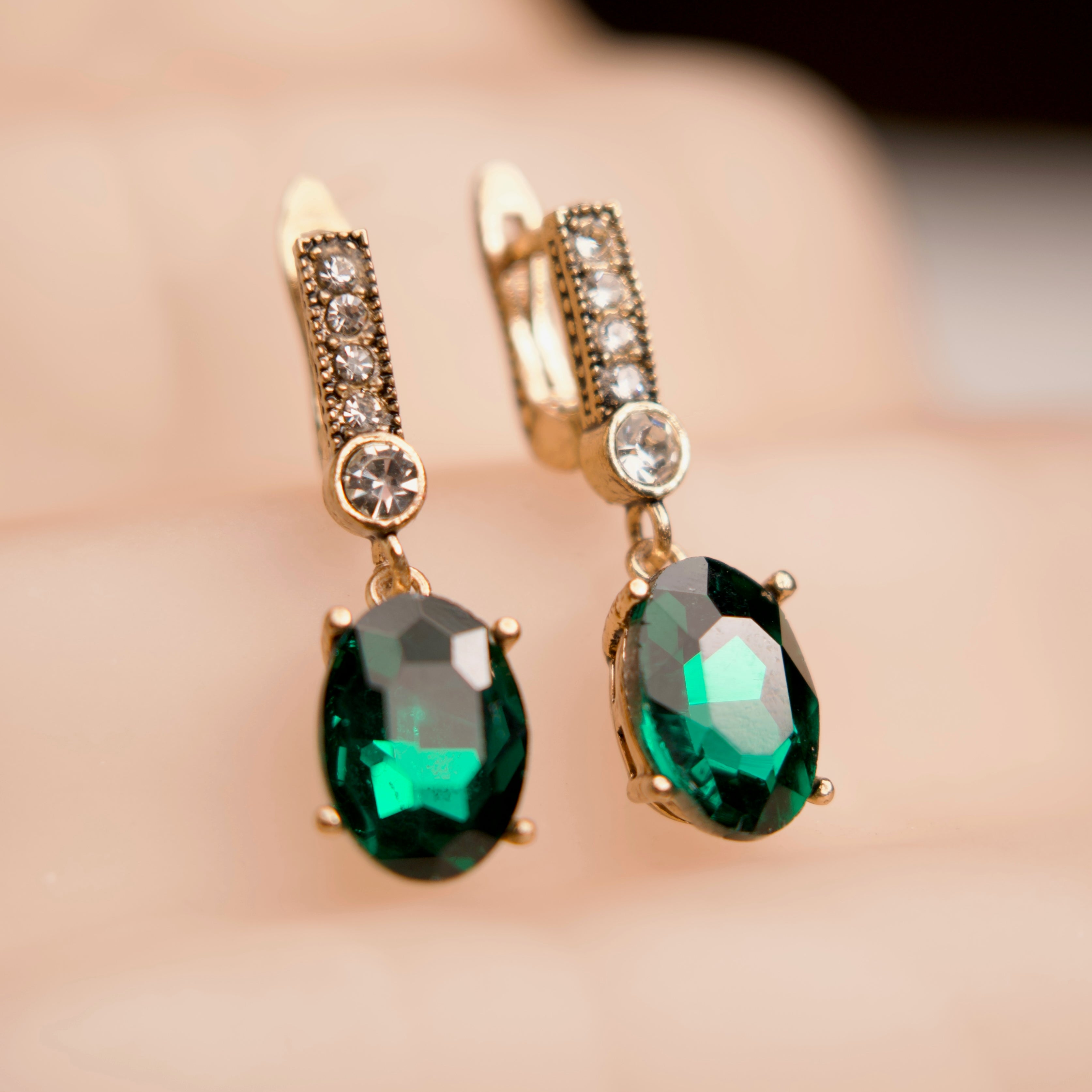 Gold earrings with green gemstones on a blurred background