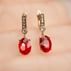 Gold earrings with red gemstones on a soft pink background