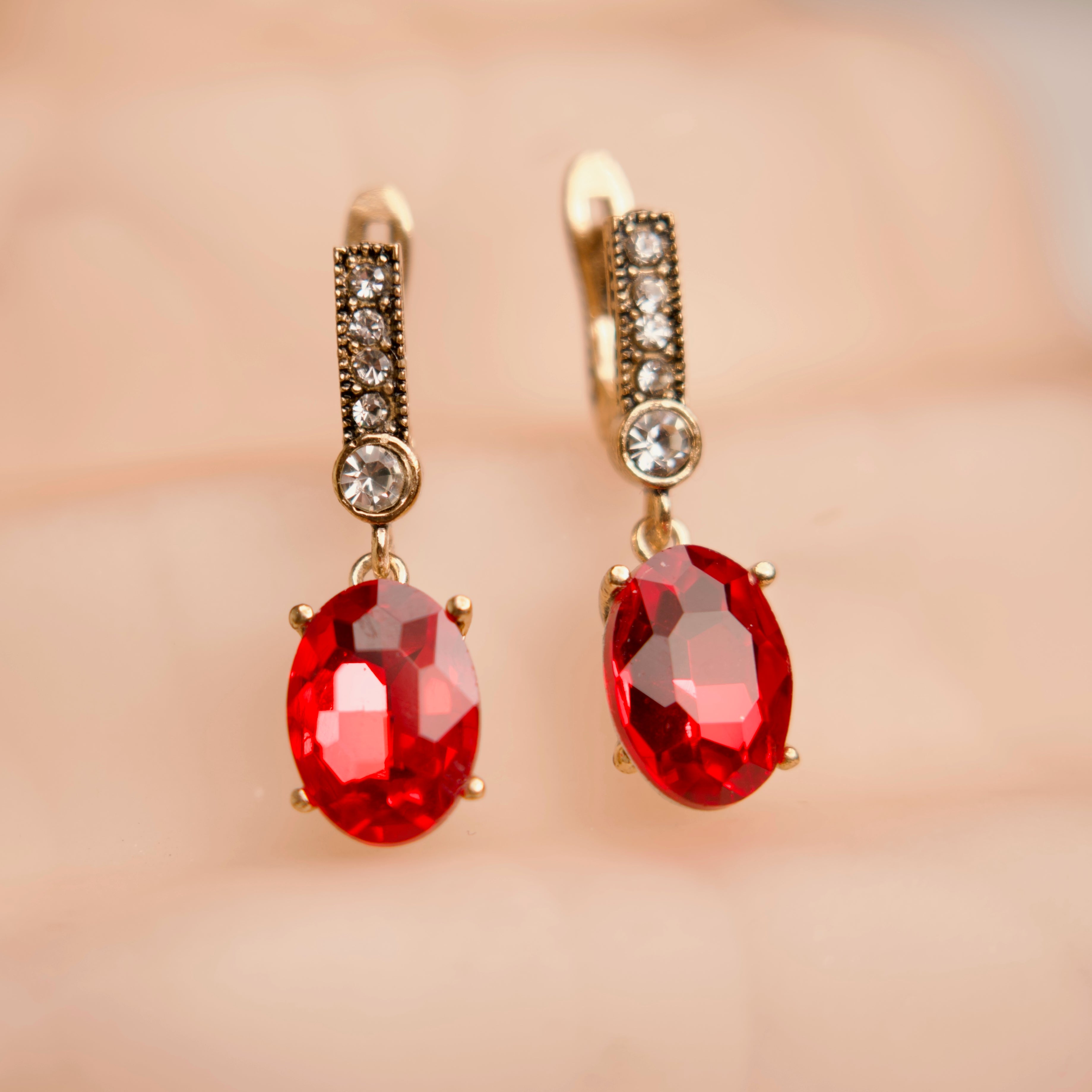 Gold earrings with red gemstones on a soft pink background