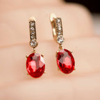 Gold earrings with red gemstones on a blurred background