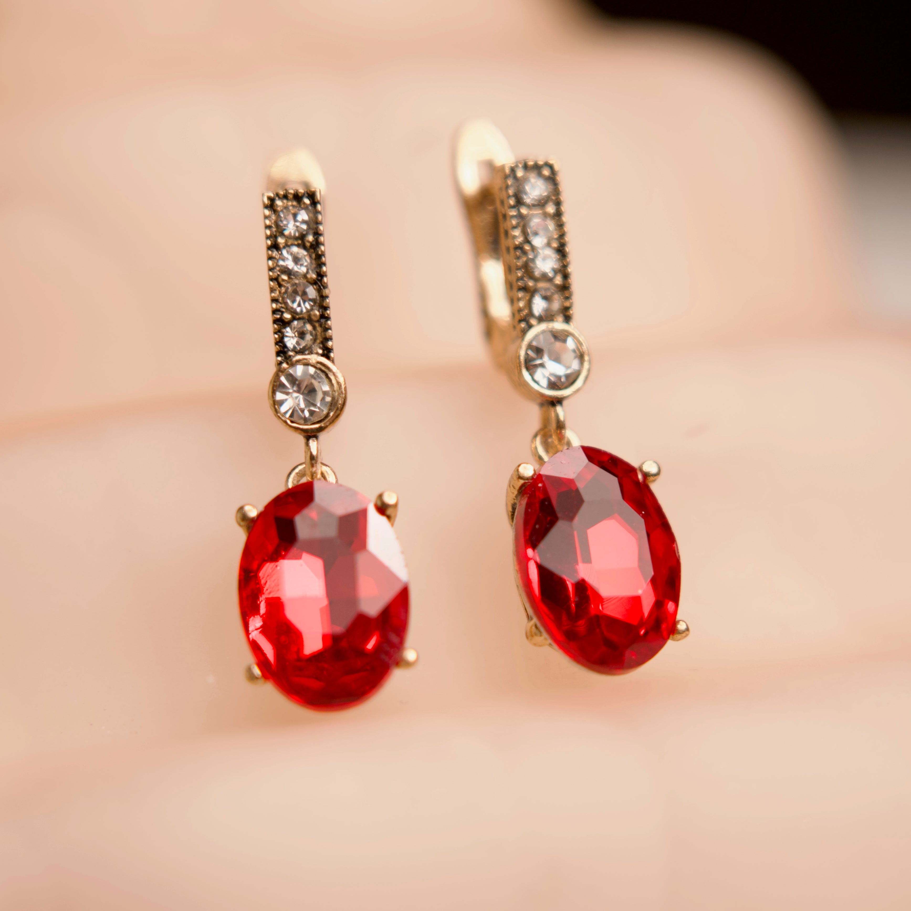 Gold earrings with red gemstones on a blurred background