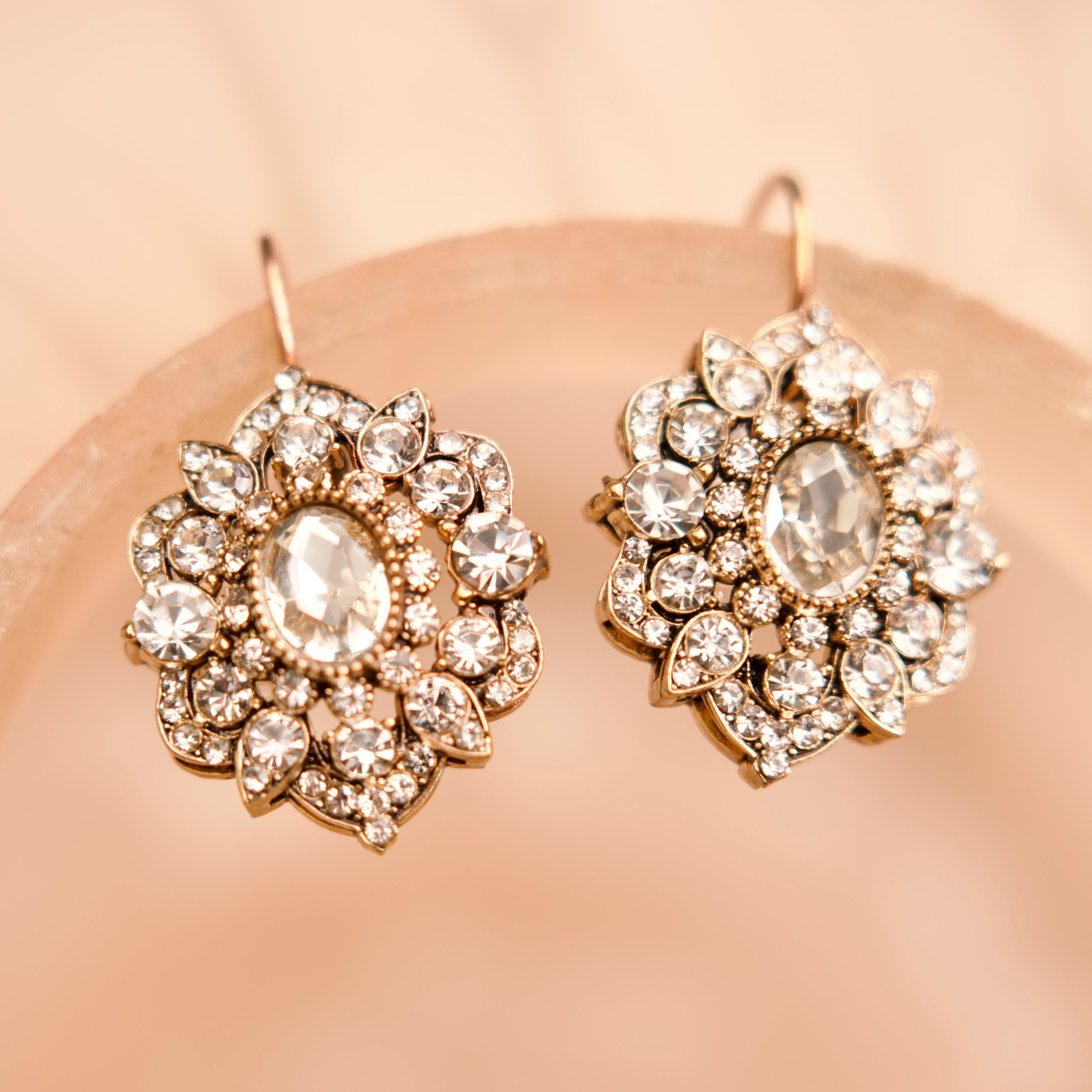 Pair of ornate earrings with clear gemstones on a beige background