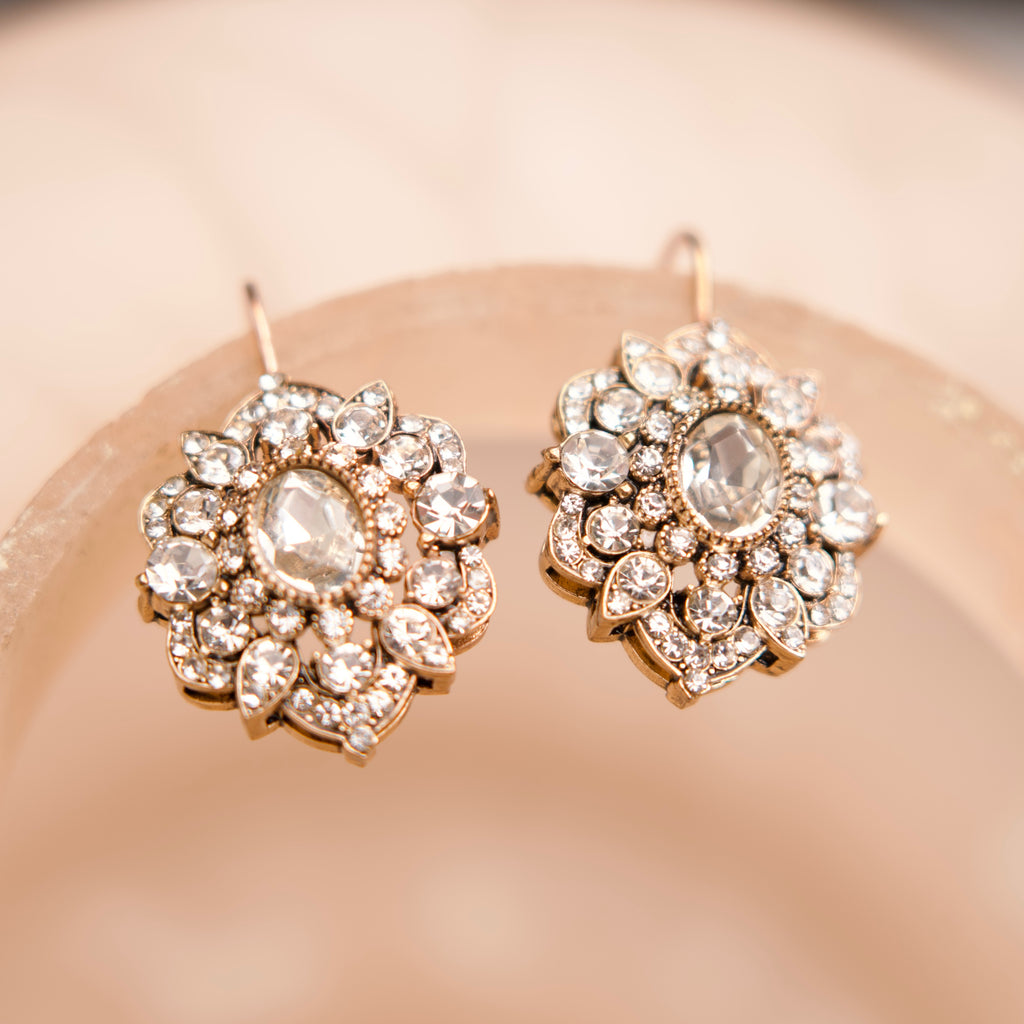 Pair of ornate earrings with gemstones on a soft pink background