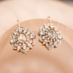 Pair of ornate earrings with gemstones on a soft pink background