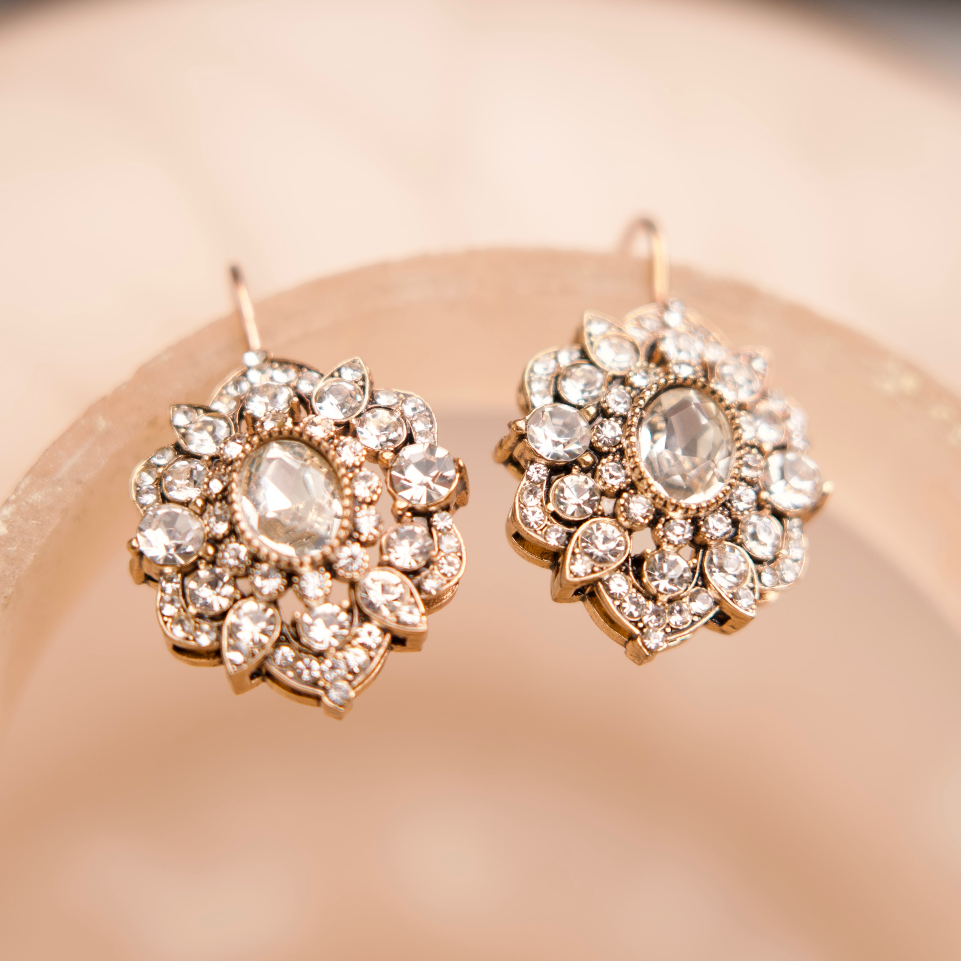 Pair of ornate earrings with gemstones on a soft pink background