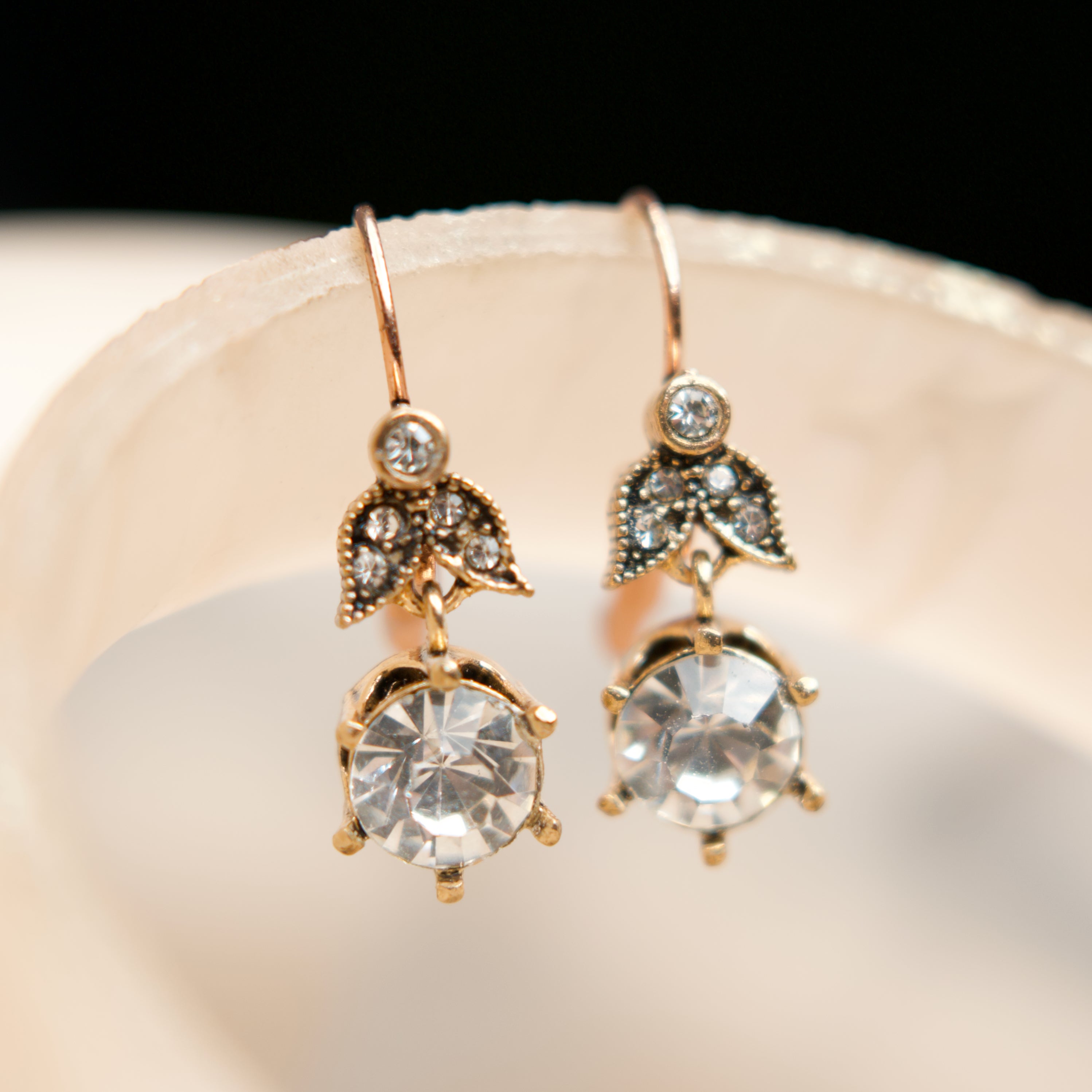 Gold earrings with clear gemstones on a white dish