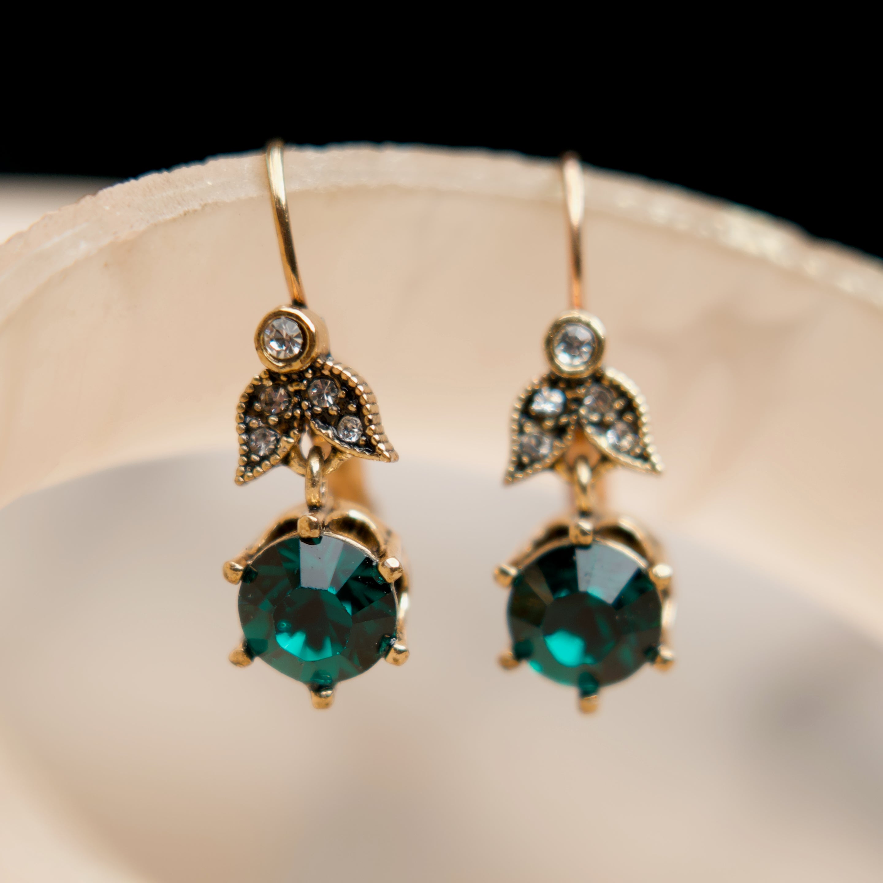 Gold earrings with green gemstones on a beige stand against a black background
