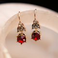 Gold earrings with red gemstones on a beige surface