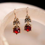 Gold earrings with red gemstones on a beige surface