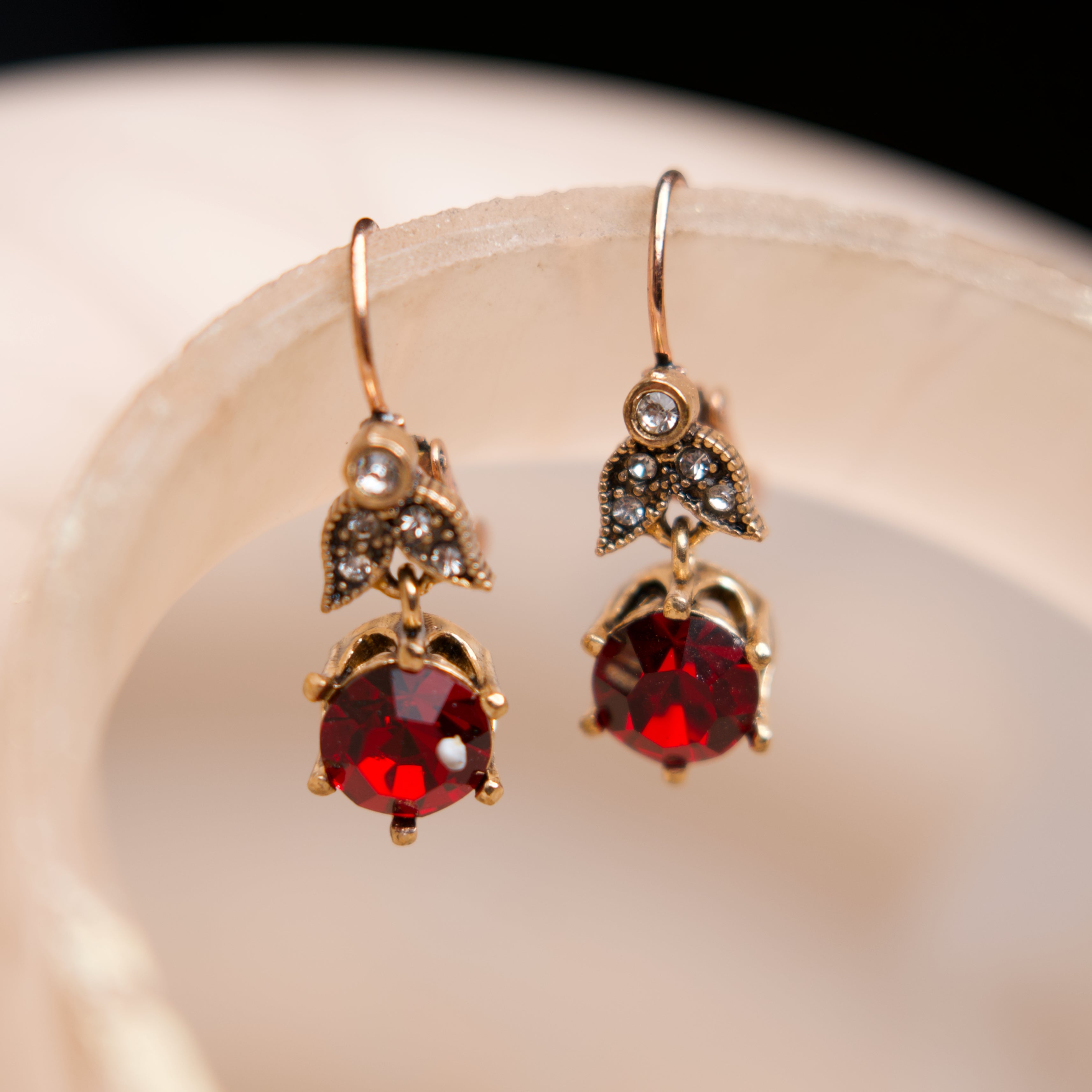 Gold earrings with red gemstones on a beige surface