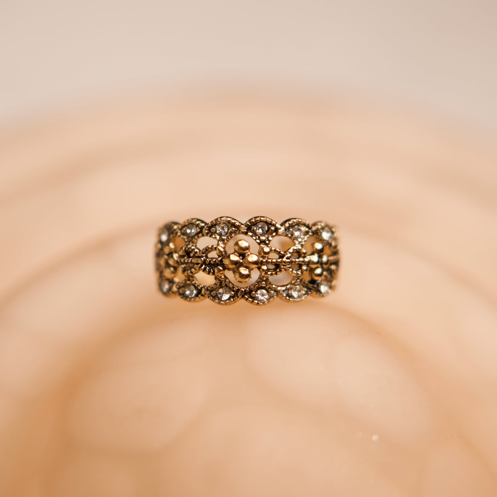 Gold ring with intricate design on a beige background