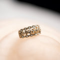 Gold ring with intricate design on a soft pink background