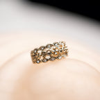 Gold ring with intricate design on a soft pink background