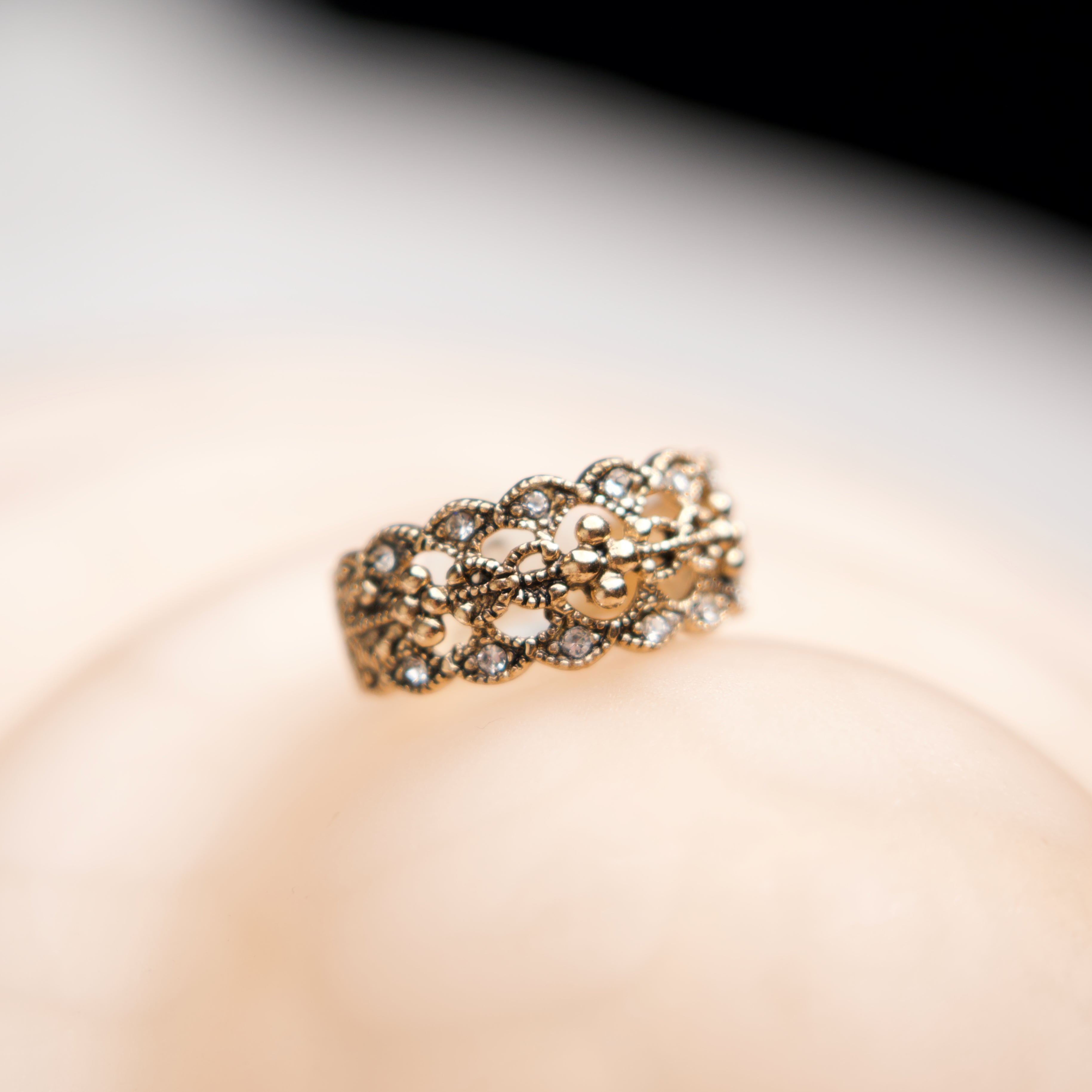 Gold ring with intricate design on a soft pink background