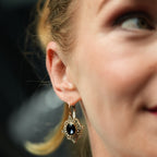 Close-up of a woman wearing a decorative earring with a dark gemstone against a blurred background