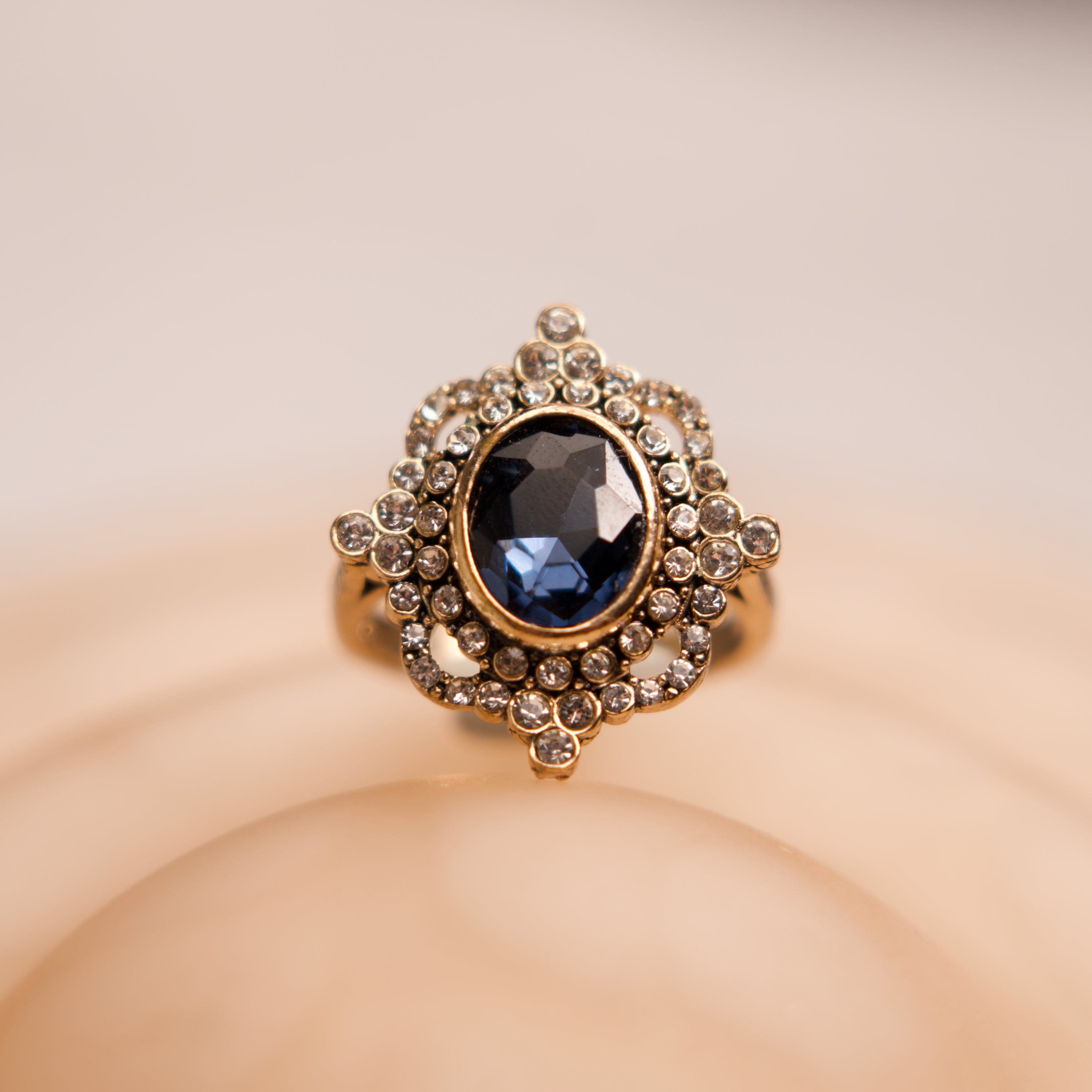 Decorative ring with a blue gemstone and gold accents on a beige background