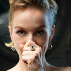Woman with a ring on her finger holding a white string against a dark background