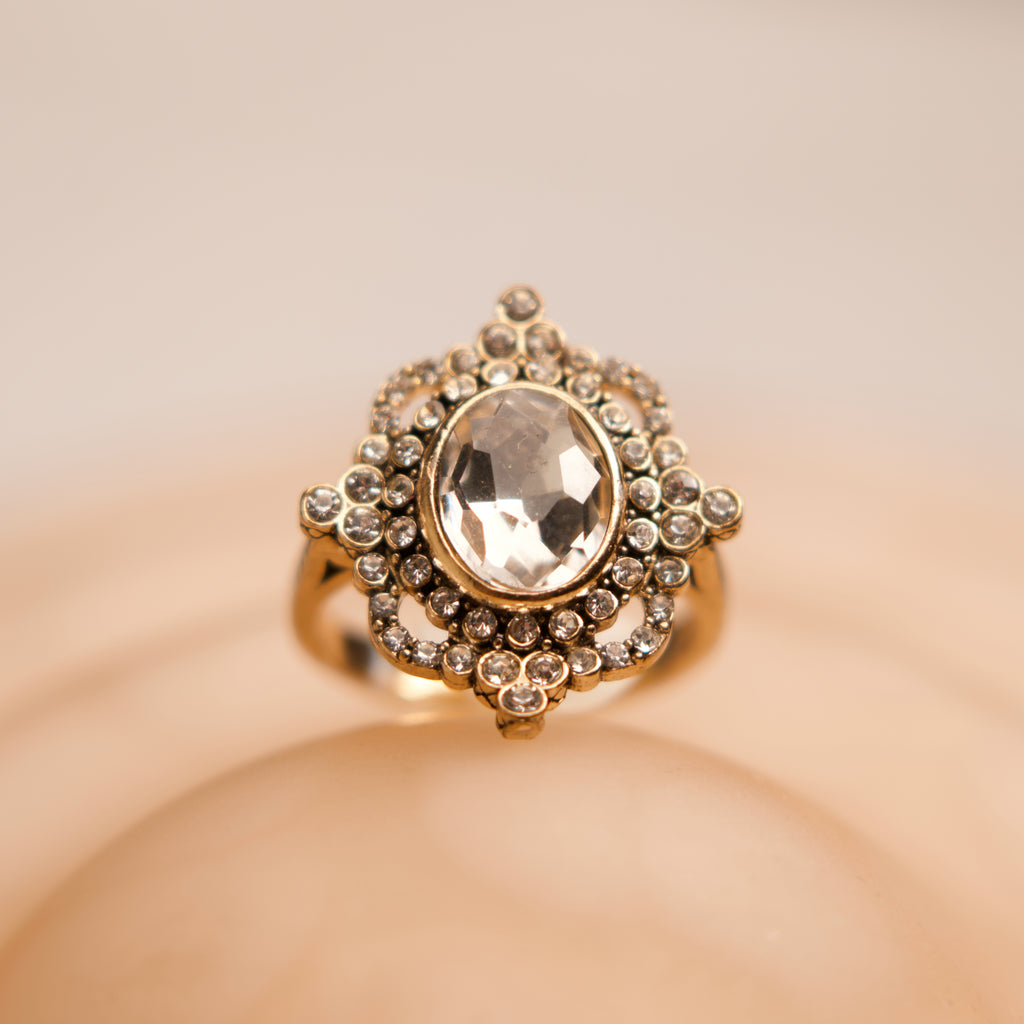 Gold ring with a large central gemstone on a beige background