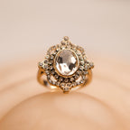 Gold ring with a large central gemstone on a beige background