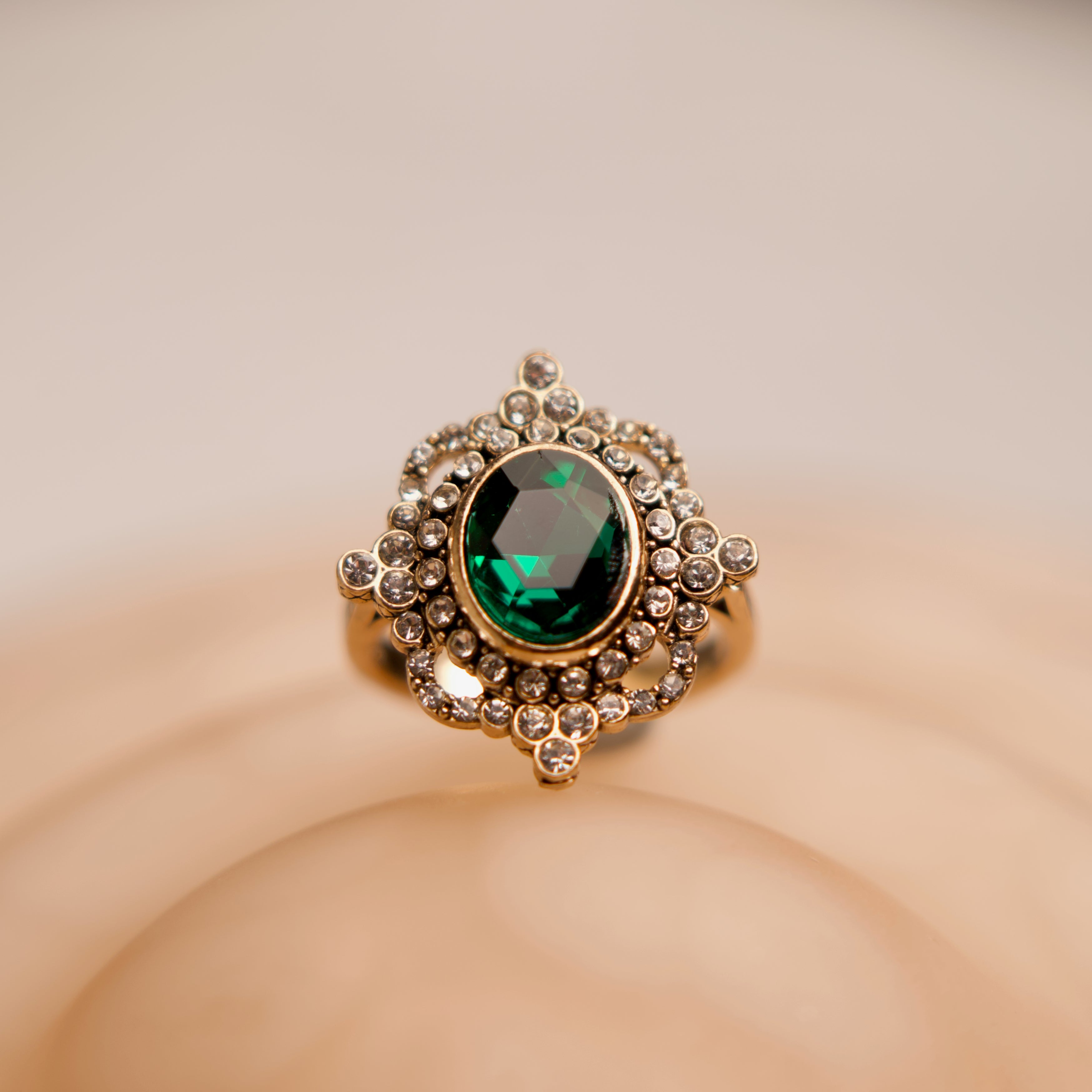 Gold ring with a green gemstone on a beige background