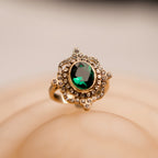 Gold ring with a green gemstone on a beige background