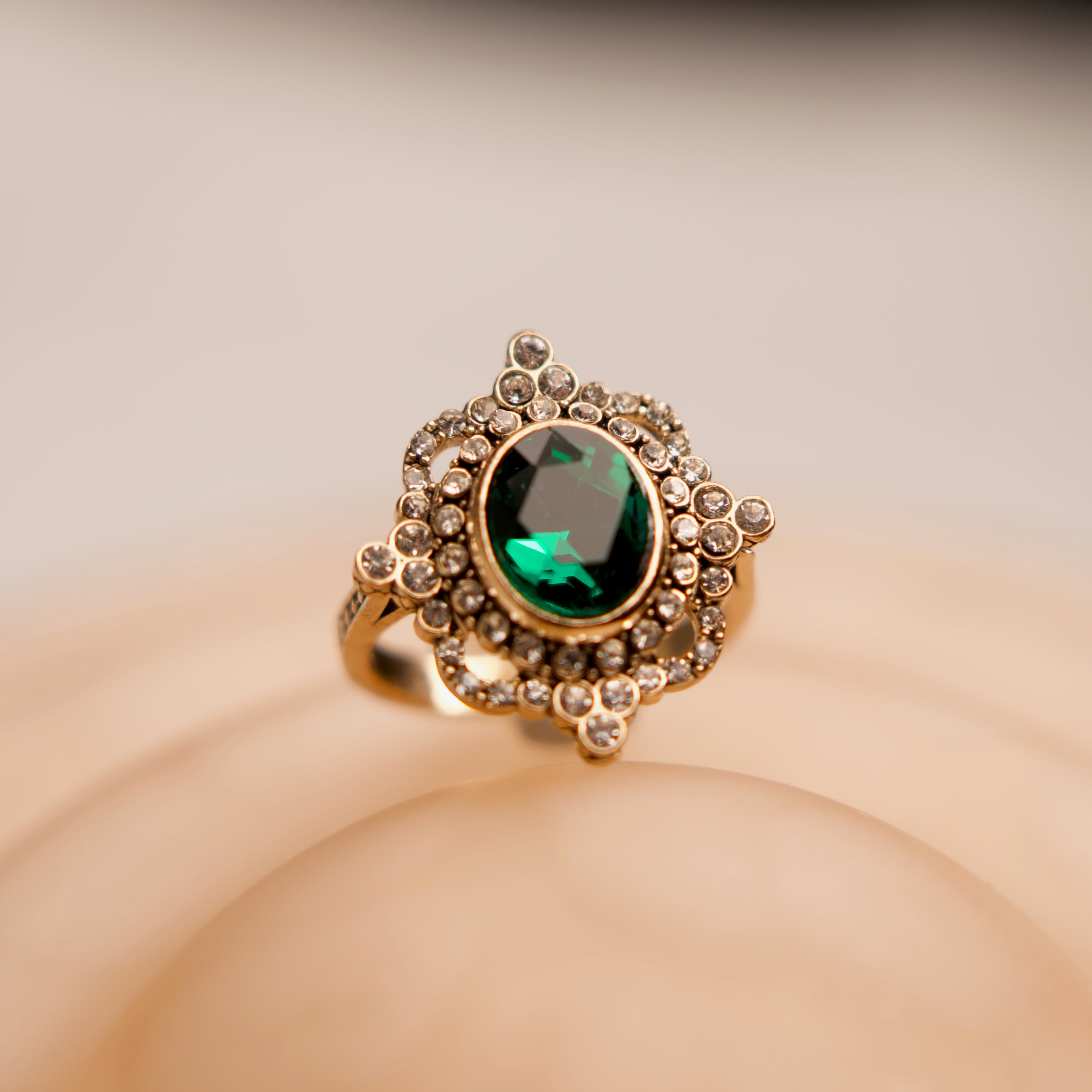 Gold ring with a green gemstone on a beige background