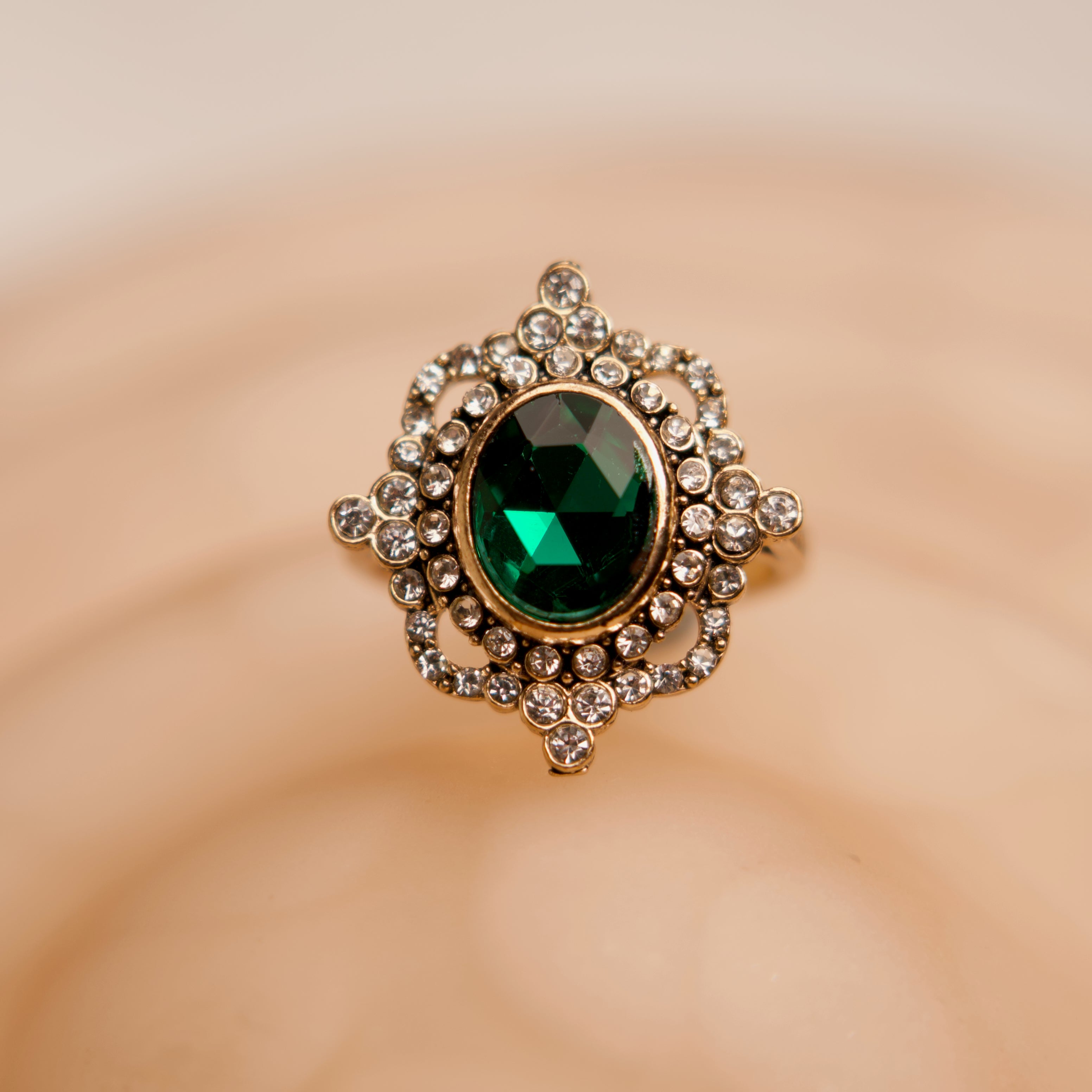 Decorative brooch with a green gemstone and gold detailing on a beige background